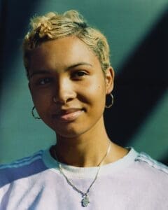 http://Close-up%20portrait%20of%20a%20person%20named%20Star%20with%20blonde%20hair,%20wearing%20a%20Hamsa%20necklace%20in%20Stratford,%20East%20London;%20a%20natural%20light%20character%20study%20by%20British%20photographer%20Ben%20Stockley.