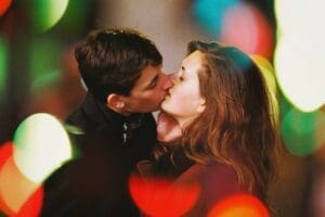 http://Close-up%20of%20a%20young%20couple%20kissing%20passionately%20at%20night,%20framed%20by%20large,%20vibrant%20red%20and%20green%20bokeh%20lights;%20a%20candid%20moment%20captured%20on%20a%20busy%20high%20street%20for%20the%20Ben%20Stockley%20Night%20Walking%20photography%20project.