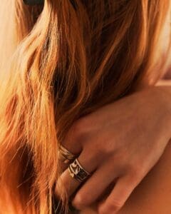 http://Close-up%20of%20reddish-blonde%20hair%20with%20a%20hand%20wearing%20a%20detailed%20silver%20ring%20nestled%20within%20it,%20in%20warm%20lighting.