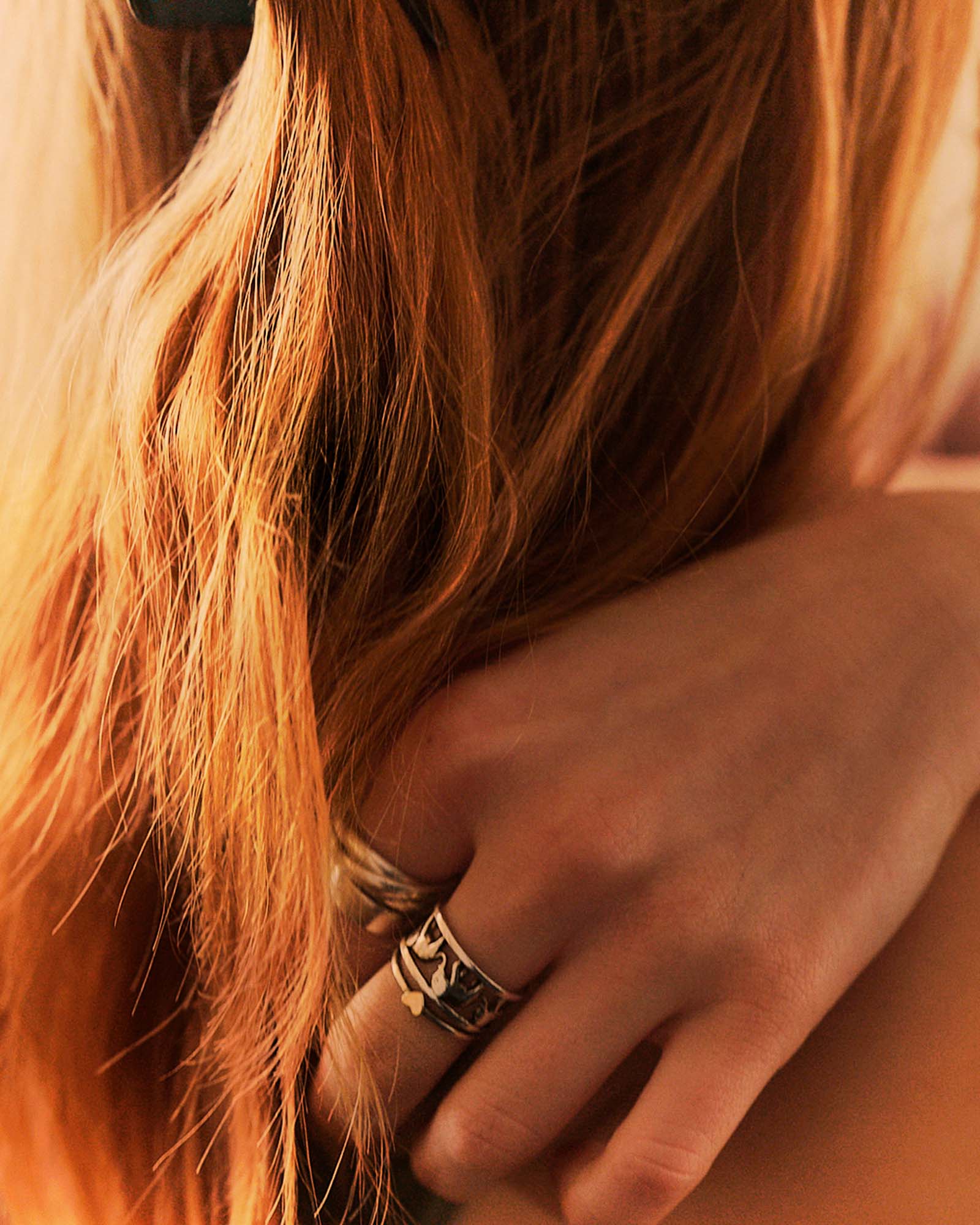 http://Close-up%20of%20reddish-blonde%20hair%20with%20a%20hand%20wearing%20a%20detailed%20silver%20ring%20nestled%20within%20it,%20in%20warm%20lighting.