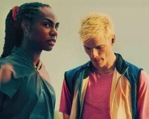 http://Close-up%20of%20a%20woman%20with%20braids%20looking%20at%20the%20camera%20and%20a%20blonde%20man%20looking%20down,%20both%20wearing%20earbuds,%20against%20a%20pale%20sky.